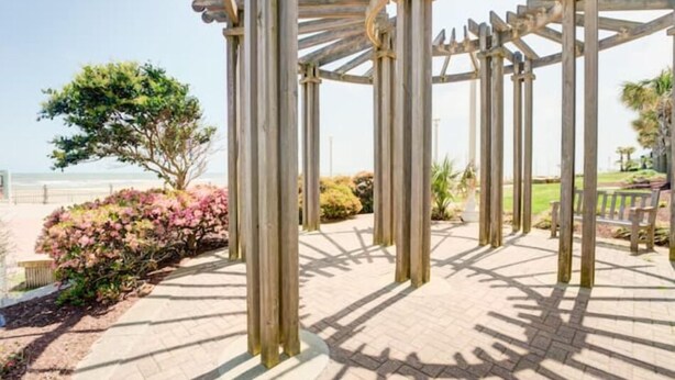 A wooden pergola structure with a clear view of the beach and ocean in the background. - Sunny Days Beach Studio on the Boardwalk w/Pool (Virginia Beach)
