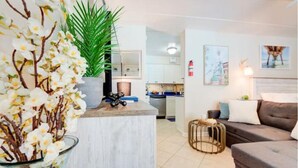 A modern living room with a grey sofa, a glass coffee table, and a potted plant. - Sunny Days Beach Studio on the Boardwalk w/Pool (Virginia Beach)