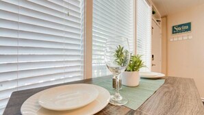A dining table with plates and a glass, a potted plant, and a sign on the wall. - Sunny Days Beach Studio on the Boardwalk w/Pool (Virginia Beach)