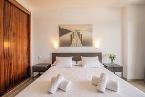 A hotel room with a large bed, two bedside tables, a wooden wardrobe, and a painting on the wall.
