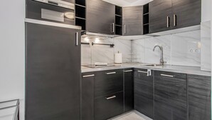 Una cocina moderna con armarios oscuros, una campana extractora de acero inoxidable, un fregadero y un reloj en la pared.