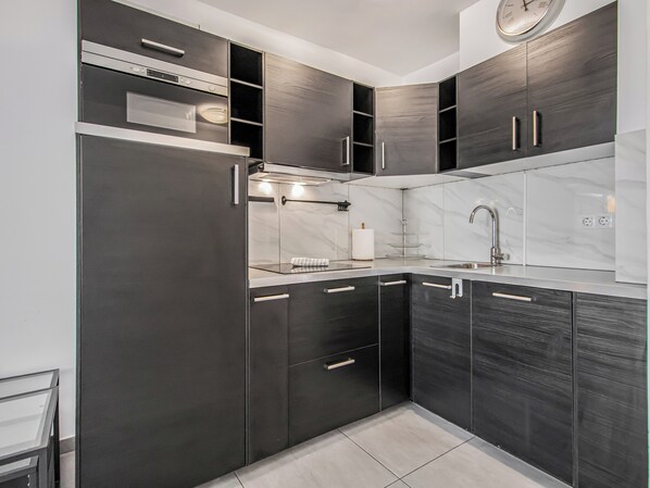 A modern kitchen with dark cabinetry, a stainless steel range hood, a sink, and a clock on the wall.