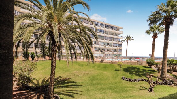 Un hotel con piscina, palmeras y vista al océano.