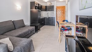 Un espacio habitable compacto con sofá, una mesa de comedor con sillas, una pequeña cocina y una puerta de madera.