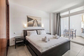 A hotel room with a large bed, a nightstand, a bedside table, a window with curtains, and a view of the outdoors.