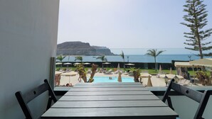 A view from a balcony overlooking a pool area with lounge chairs and umbrellas, a clear sky, and a distant view of the sea and a hill. - Cura Marina Seafront Playa del Cura (Mogán)