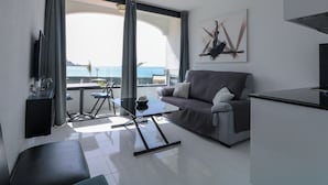 A modern living room with a sofa, a dining table, and a TV. There is a large window with a view of the sea. - Cura Marina Seafront Playa del Cura (Mogán)