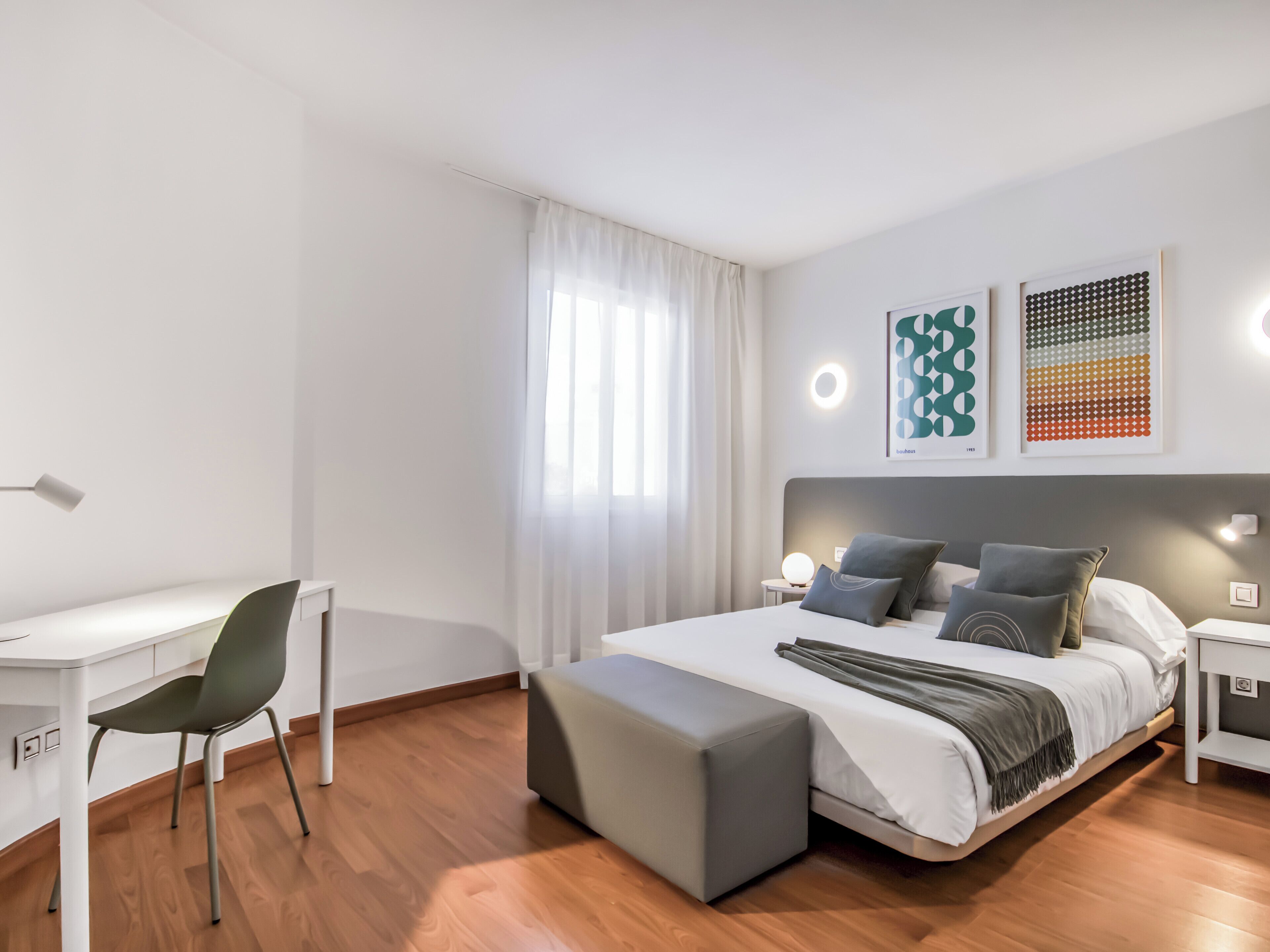 A modern hotel room with a bed, a desk, a chair, and a large window with curtains.