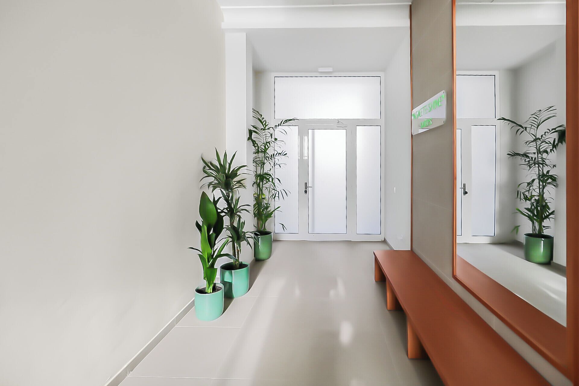 A hallway with a bench, potted plants, and a door with a sign.