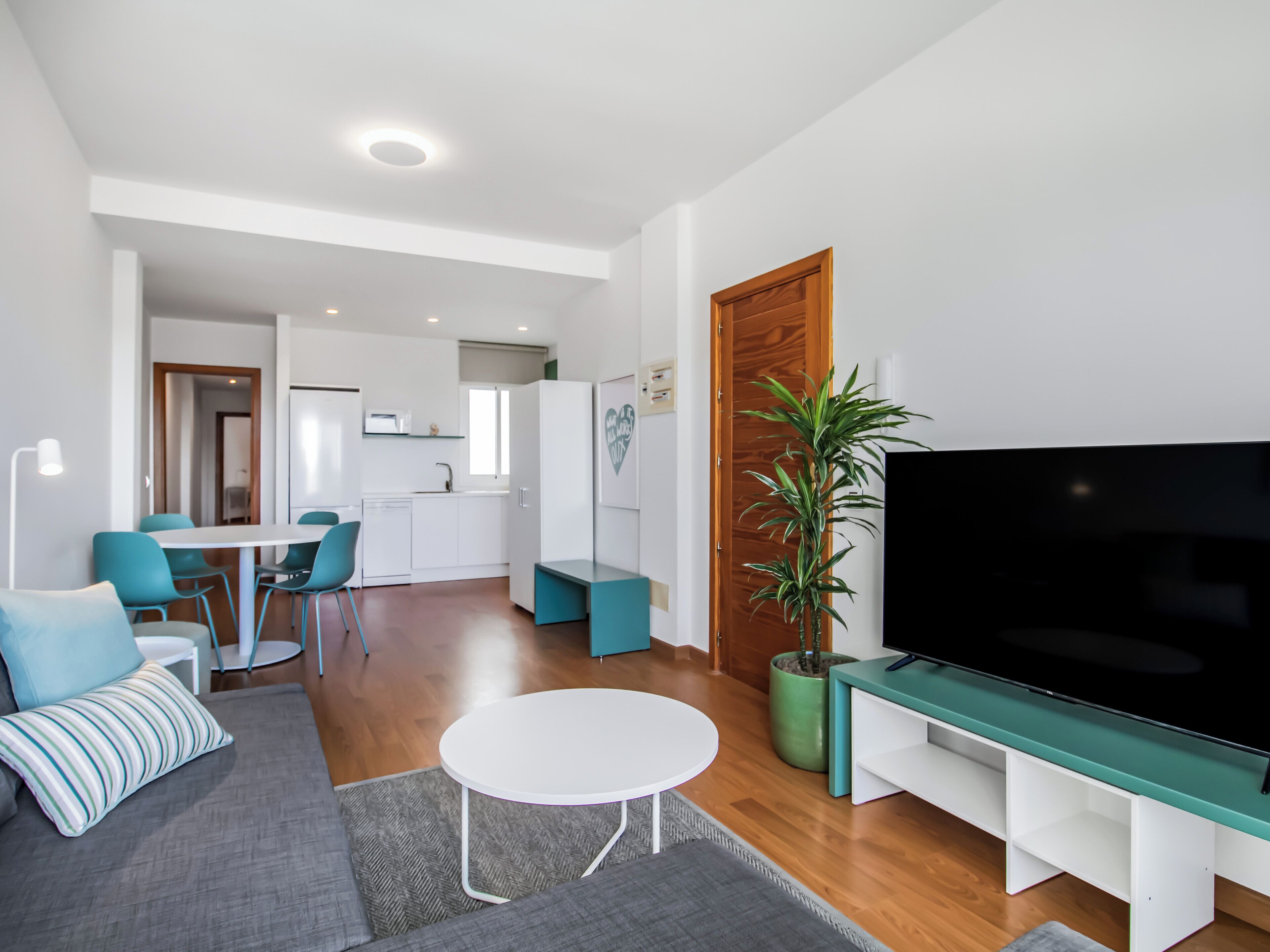 A modern living room with a sofa, a TV, and a dining area with chairs and a table.
