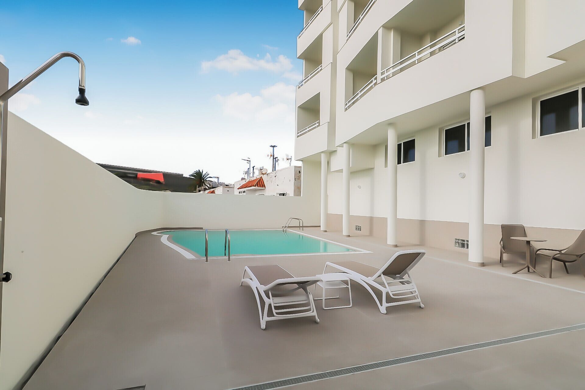 A rooftop pool area with a clear blue pool, white lounge chairs, and a modern building with balconies.