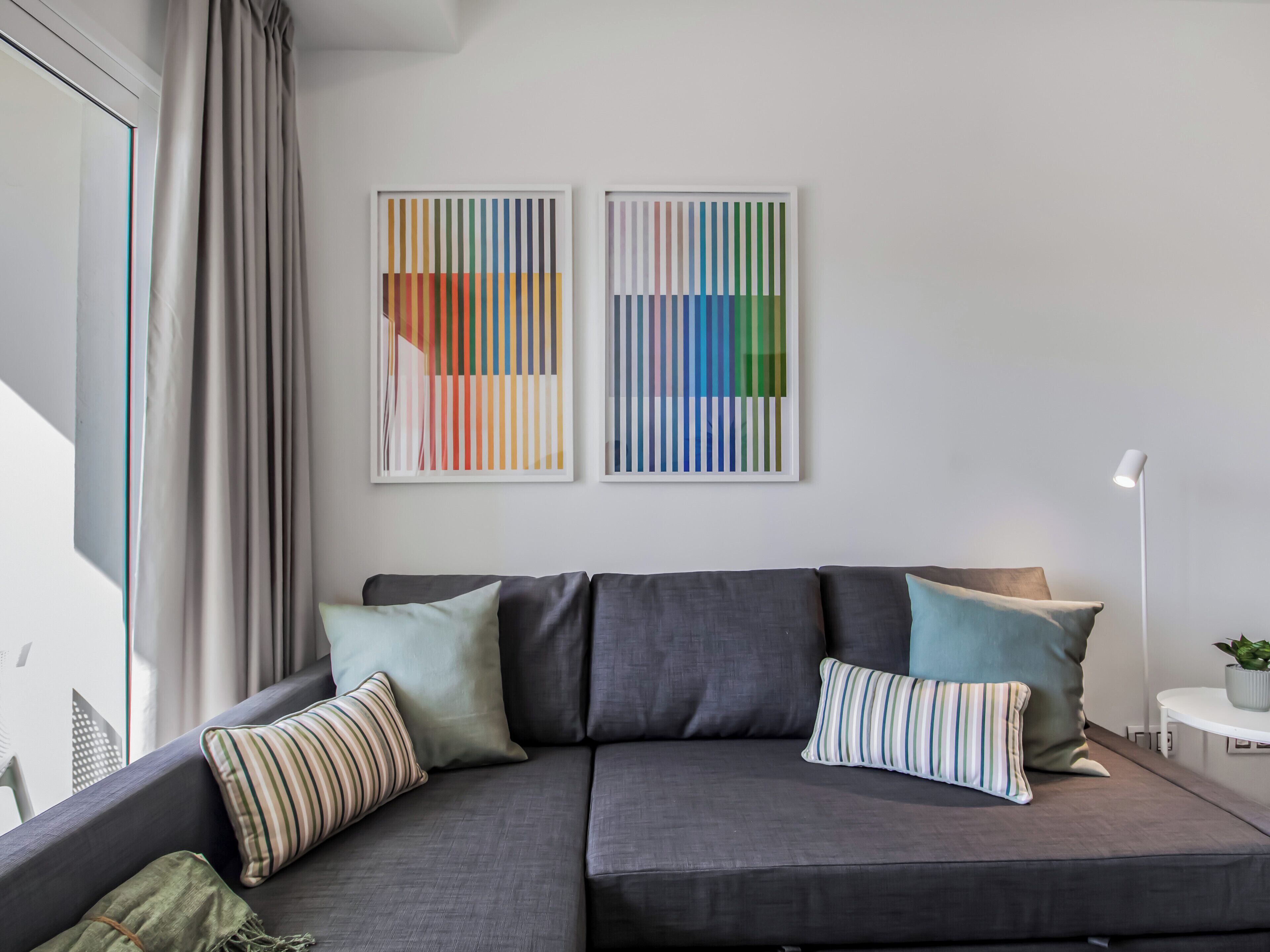 A modern living room with a grey sofa, striped pillows, and two abstract paintings on the wall.
