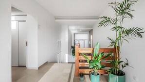 Een gang met een houten bankje, planten in potten en een witte deur aan het einde.