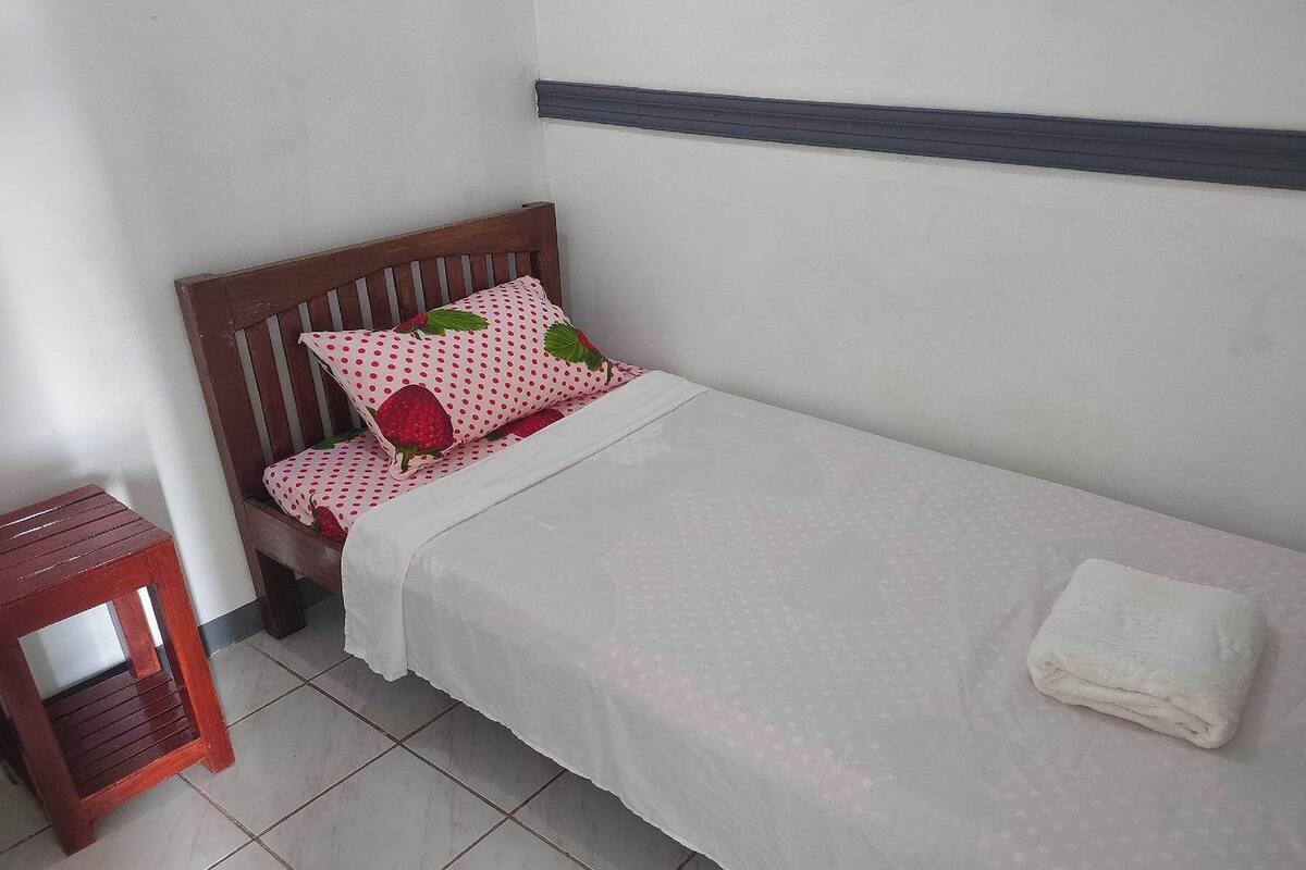 A small, neatly made bed with a white bedspread and a single red and white polka dot pillow.