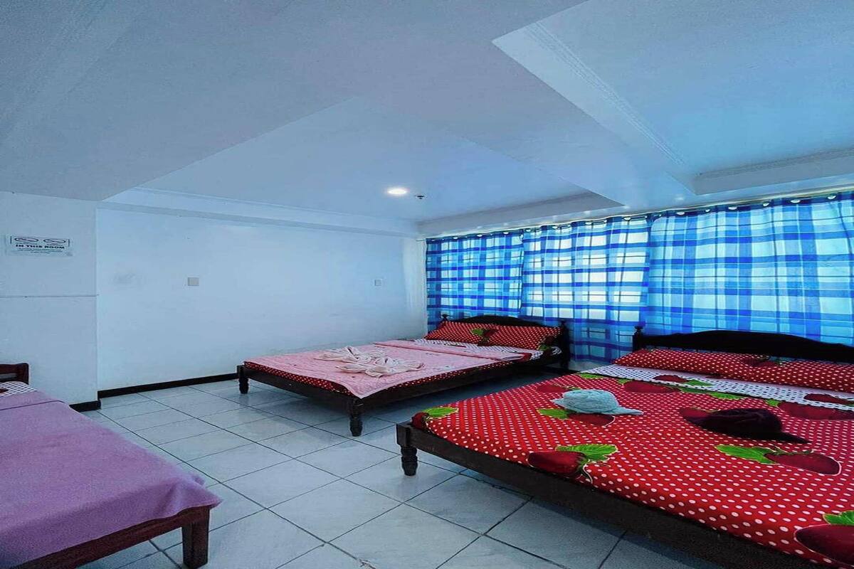 A room with two beds, a small table, and a window with blue curtains.