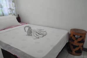 A neatly made bed with a towel in a swan shape, a round wooden stool, and a window with a tree pattern curtain. - Istroberi Inn By Zuzu (Puerto Princesa)