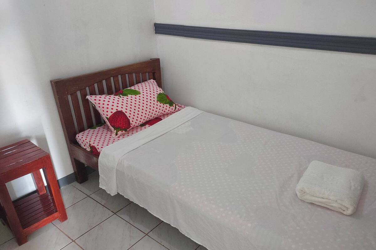 A small, neatly made bed with a white bedspread and a single pillow with a red and white polka dot pattern.