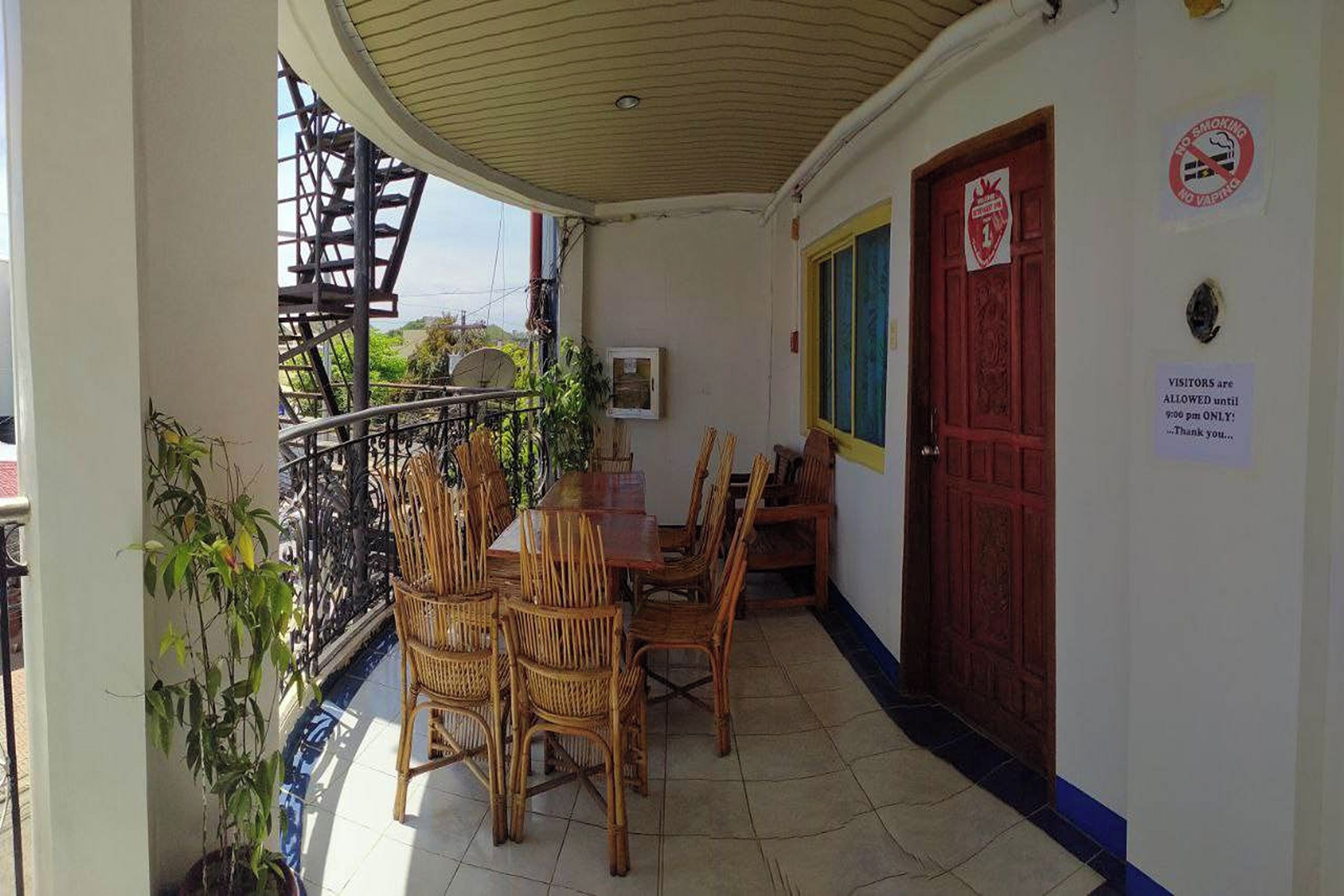 A balcony with a table and chairs, a red door, and a no smoking sign.