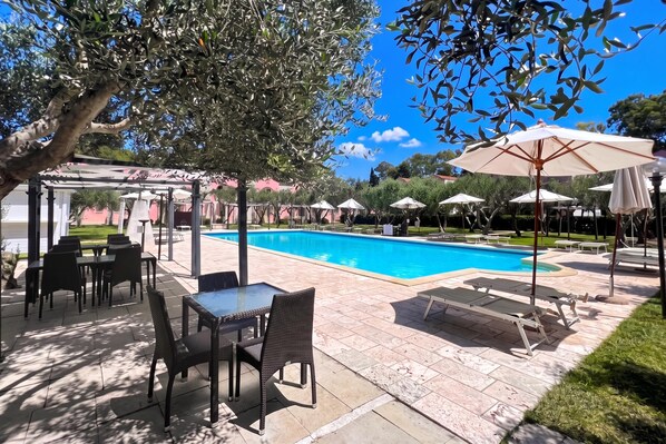 An outdoor pool area with lounge chairs and umbrellas, surrounded by a pergola and a poolside table.