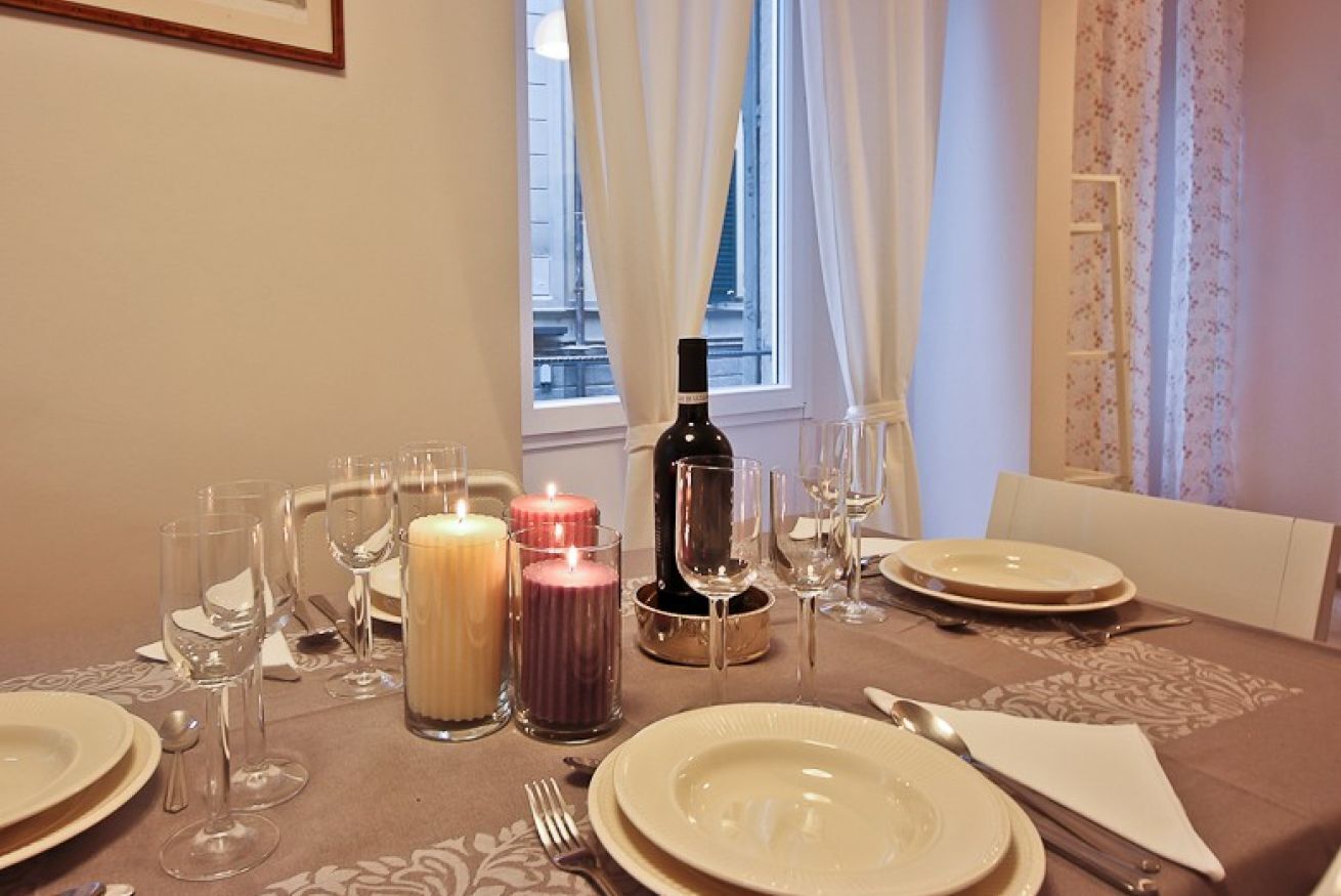 A dining table set for four with candles, wine glasses, and plates.