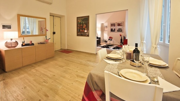 Een eethoek met een tafel gedekt voor vier personen, een houten kast en een schilderij aan de muur.