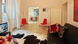 Een woonkamer met een zwarte bank, rode stoelen, een televisie en een kooidekbed.