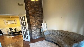 Un salon doté d’un canapé d’angle aux lignes courbes, d’un plancher en bois, d’un ventilateur de plafond et d’un mur décoratif en briques.