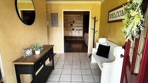 Un couloir avec un paillasson, un porte-manteau, un miroir et un panneau.