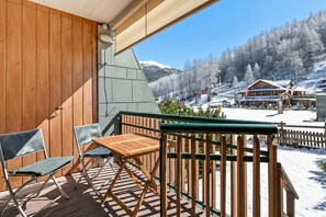 A wooden deck with a table and chairs, overlooking a snowy mountain landscape with buildings. - Theo's House with Terrace, Bardonecchia, Italy (Bardonecchia)