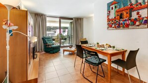 Une pièce comprenant une table à manger, des chaises, un fauteuil vert, un meuble en bois et une grande fenêtre.