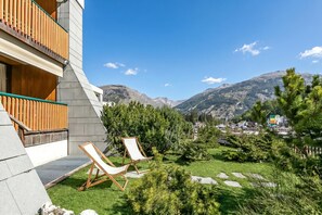 A modern building with a balcony, two lounge chairs, and a view of mountains.
