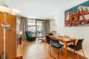 A compact living space with a dining area, a sofa, a table with chairs, and a balcony with a view.