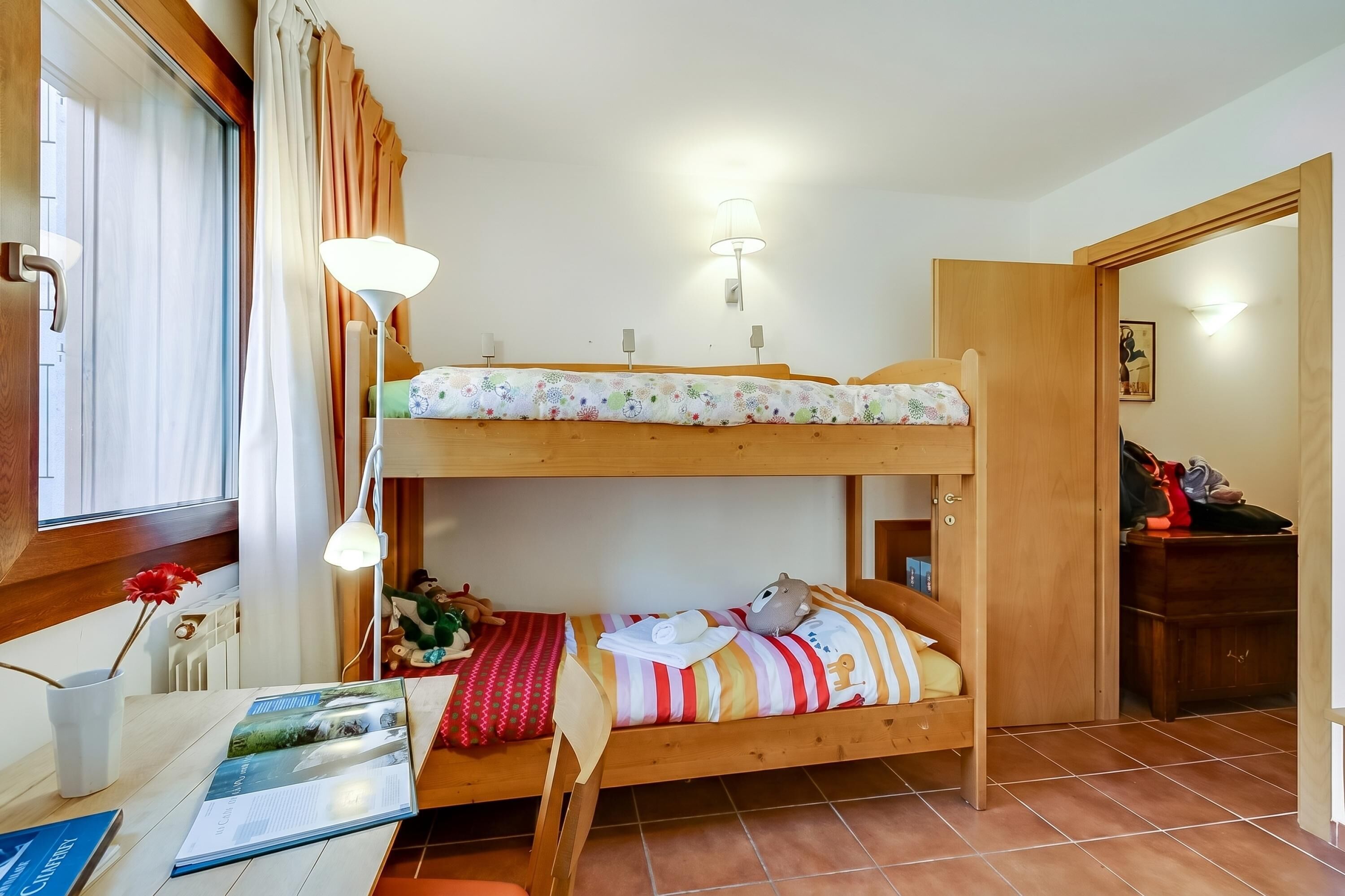 A bunk bed room with a desk, lamp, and a window with curtains.