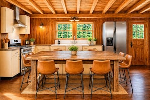 Una cocina con paredes de madera, una isla central con taburetes, electrodomésticos de acero inoxidable y un ventanal con vistas a la vegetación.