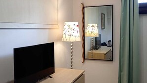 A hotel room with a flat-screen TV on a wooden dresser, a standing lamp with a floral pattern, a mirror on the wall, and a patterned rug on the floor. - Verde Mare apartment in villa with garden, oasis Saline and Playa Sol Taguali (Carrozziere)