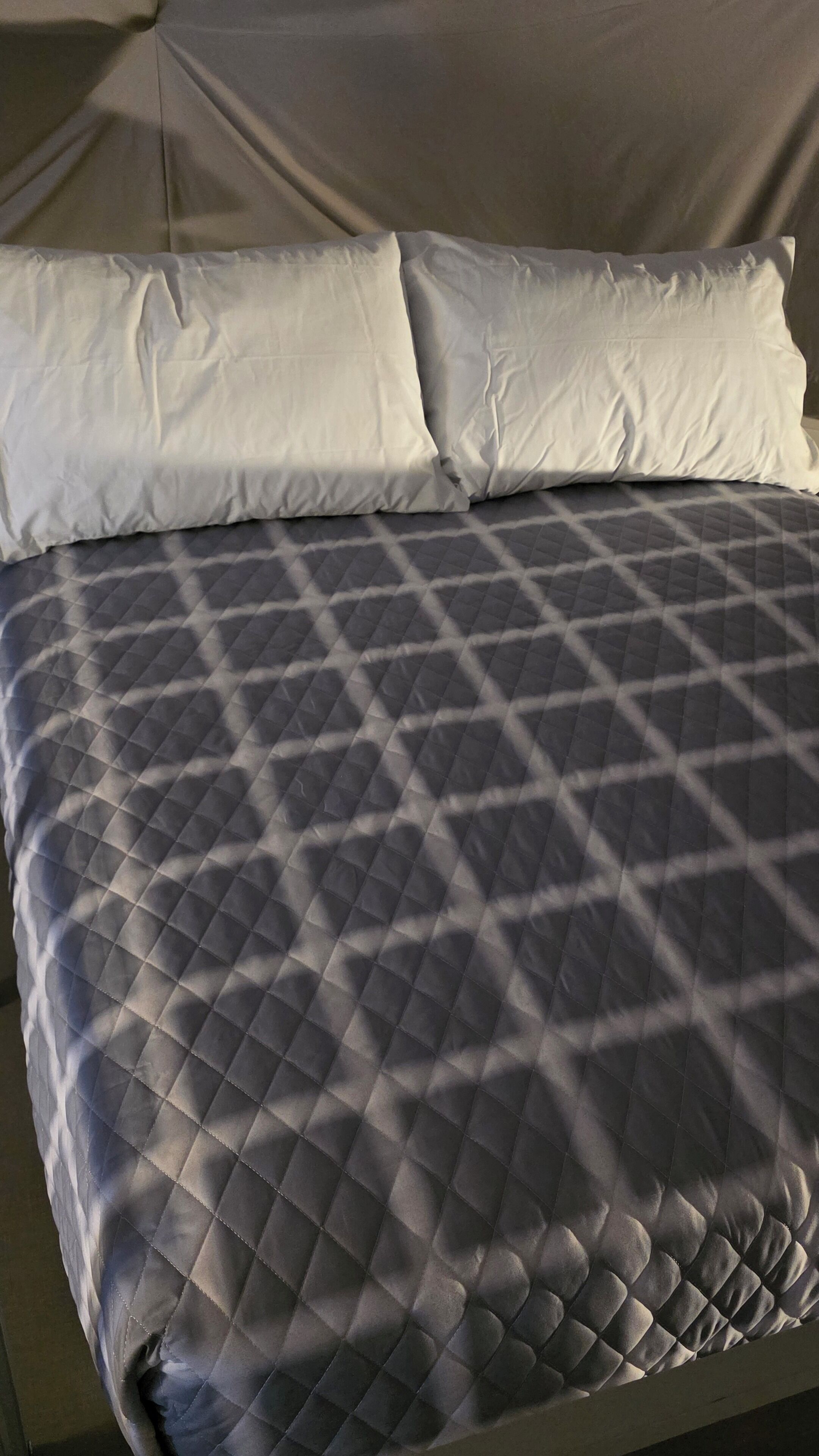 Una cama con un edredón gris acolchado y dos almohadas blancas.