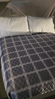 Una cama con un edredón gris acolchado y dos almohadas blancas.