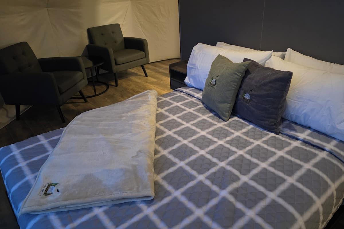A hotel room with a bed, two armchairs, and a small table.
