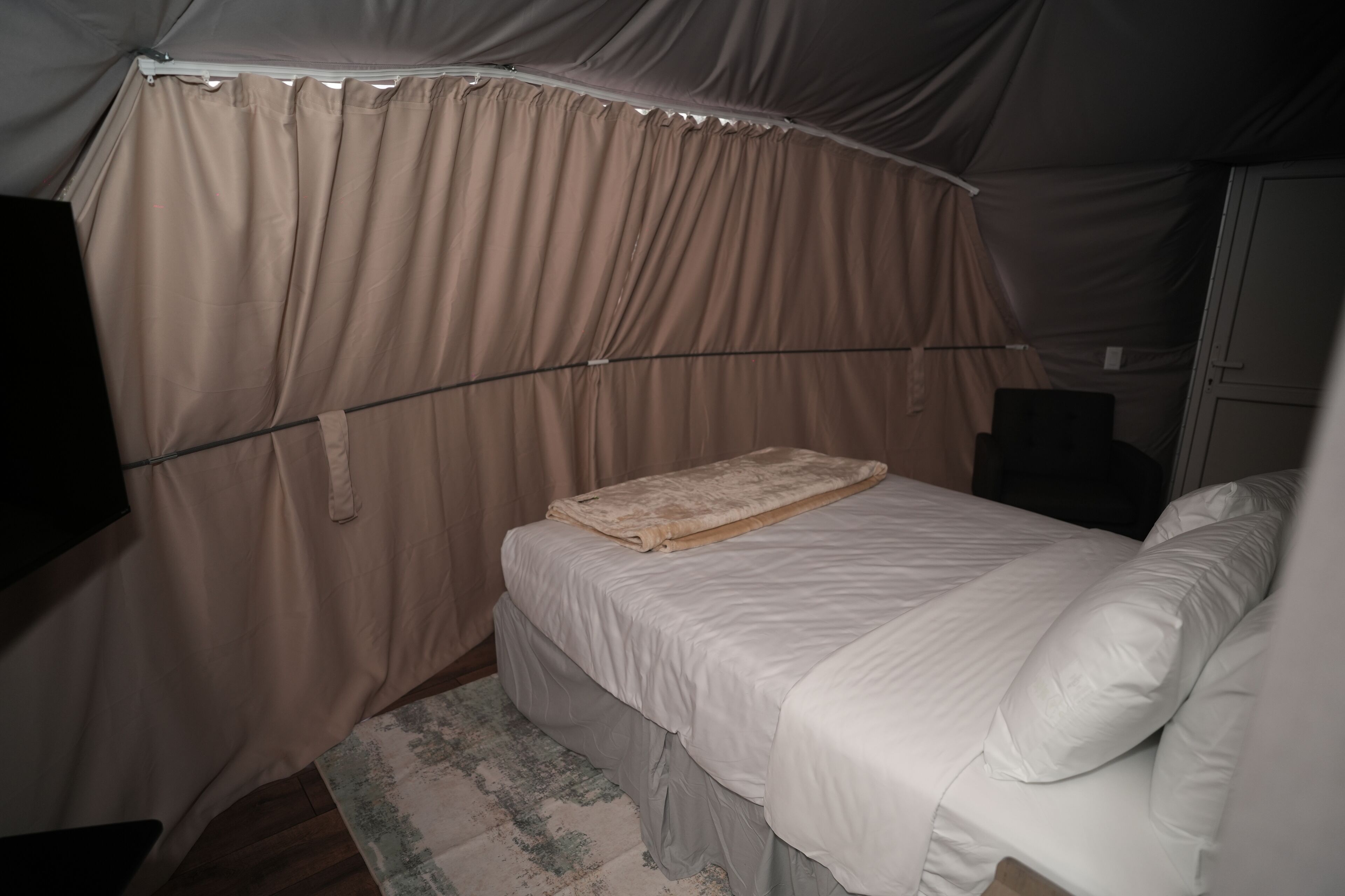 A tented room with a bed, a blanket, and a rug.