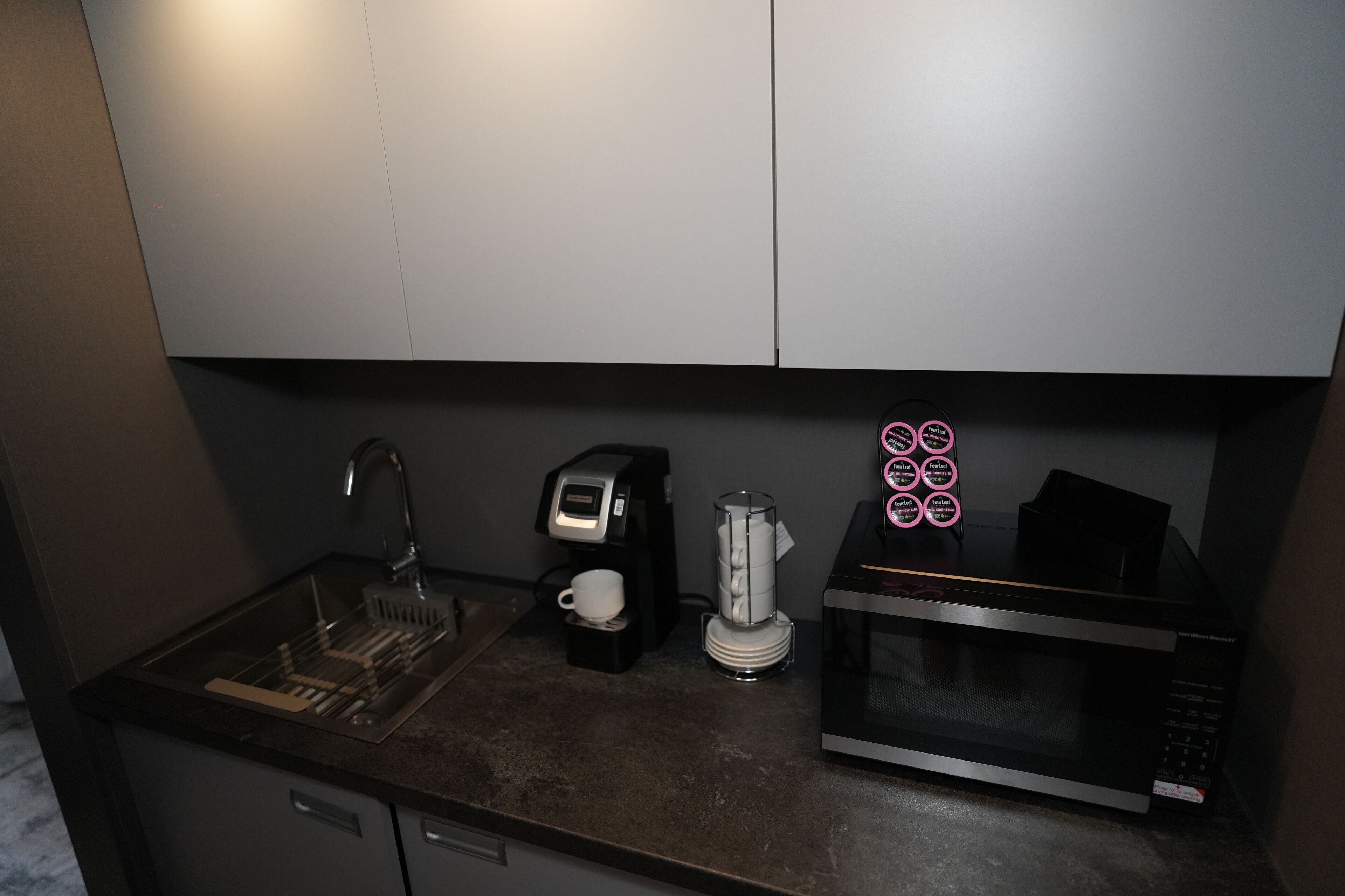 Una cocina compacta equipada con lavamanos, cafetera, hervidor y microondas.
