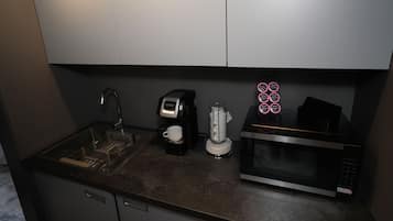 Una cocina compacta equipada con lavamanos, cafetera, hervidor y microondas.