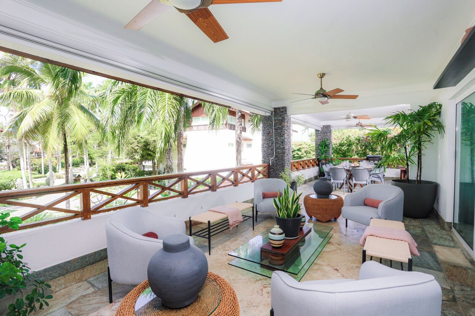 A spacious balcony with comfortable seating, a glass coffee table, and a view of palm trees.