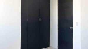 Quarto com um guarda-roupa preto grande e uma porta menor, ambos com puxadores metálicos.