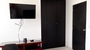 Quarto com cama, escrivaninha com cadeira, televis ão na parede e guarda-roupa.