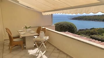 Un balcon avec une table dressée pour deux personnes, offrant une vue sur un paysage côtier.