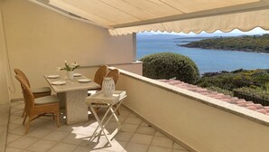 Ein Balkon mit Tisch für zwei Personen, mit Blick auf eine Küstenlandschaft.