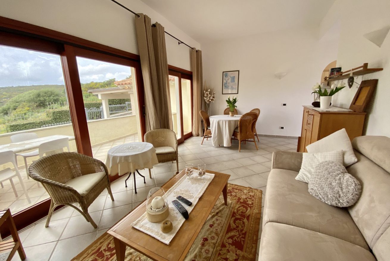 Un vaste espace de vie comprenant un canapé, une table basse et une table à manger avec des chaises. Un balcon offre une vue sur la verdure.