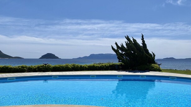 Ein Pool mit klarem, blauem Wasser, umgeben von einer angelegten Grünfläche mit Blick auf das Meer und entfernte Inseln.