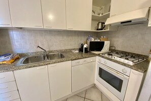 Une cuisine moderne avec des armoires blanches, un comptoir en granit, un évier en acier inoxydable, un four encastré et une cuisinière à gaz.