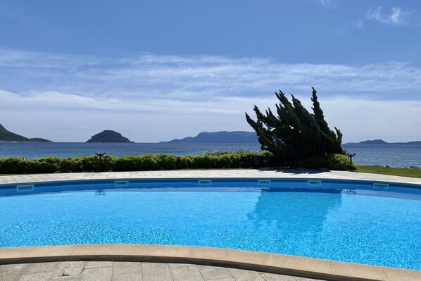 A swimming pool with clear blue water, surrounded by a landscaped area with a view of the sea and distant islands.